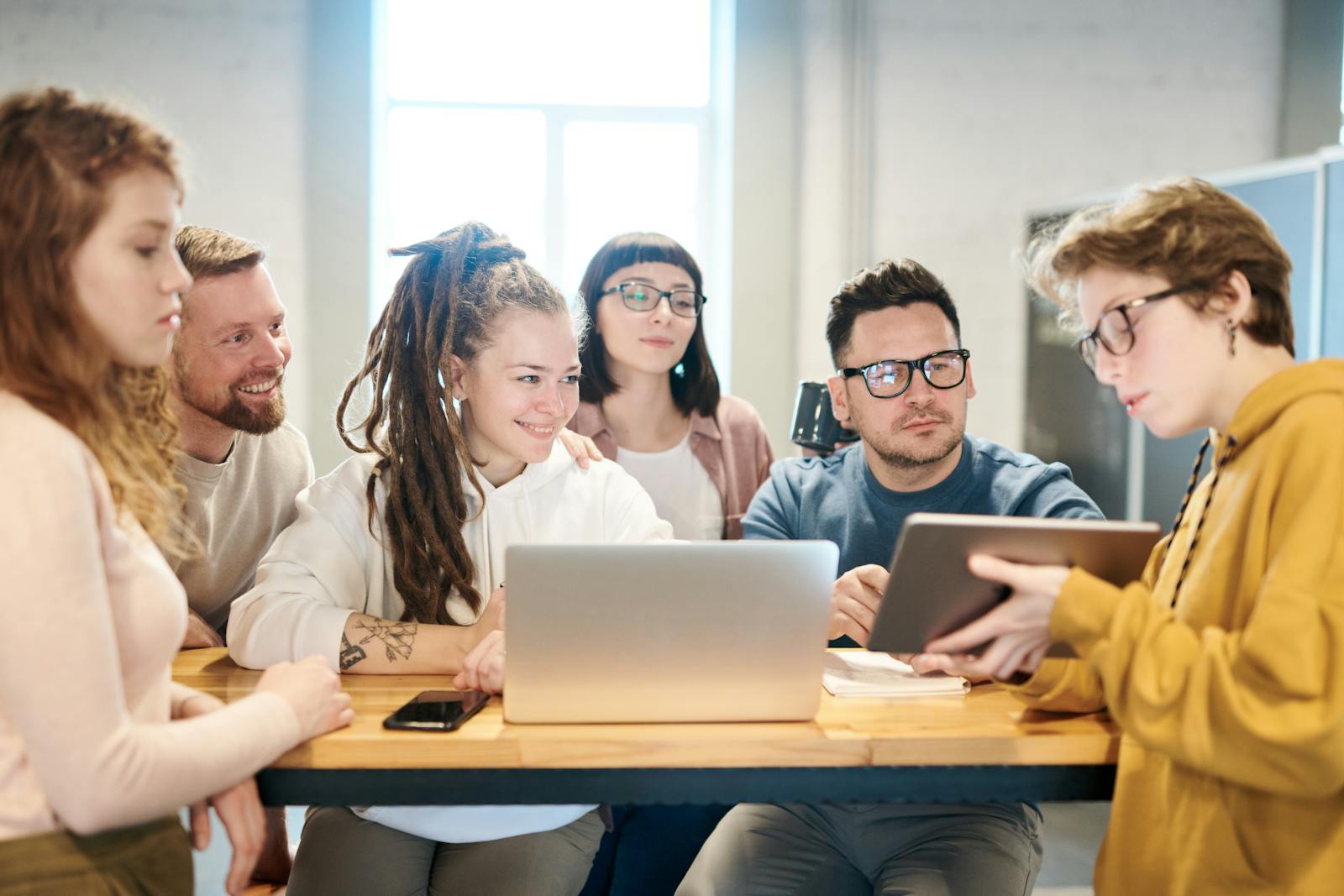 Un groupe diversifié de professionnels engagés dans une séance de brainstorming autour d'une table en bois avec la technologie présente.
