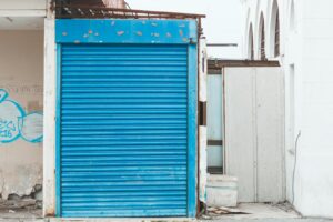 Un volet roulant bleu sur une façade de bâtiment délabrée, présentant des graffitis et des signes de dégradation.