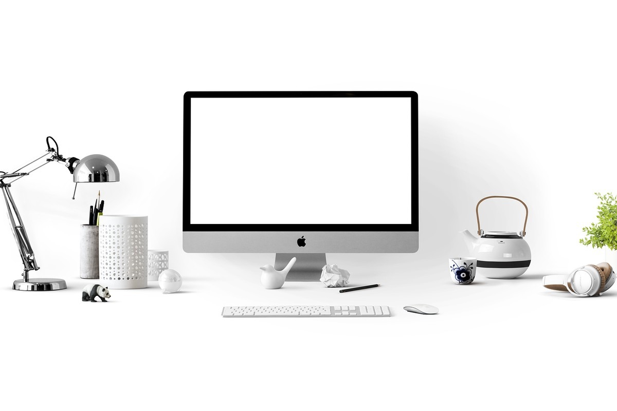 Bureau avec écran Apple, clavier, souris, lampe, tasse, théière et objets divers