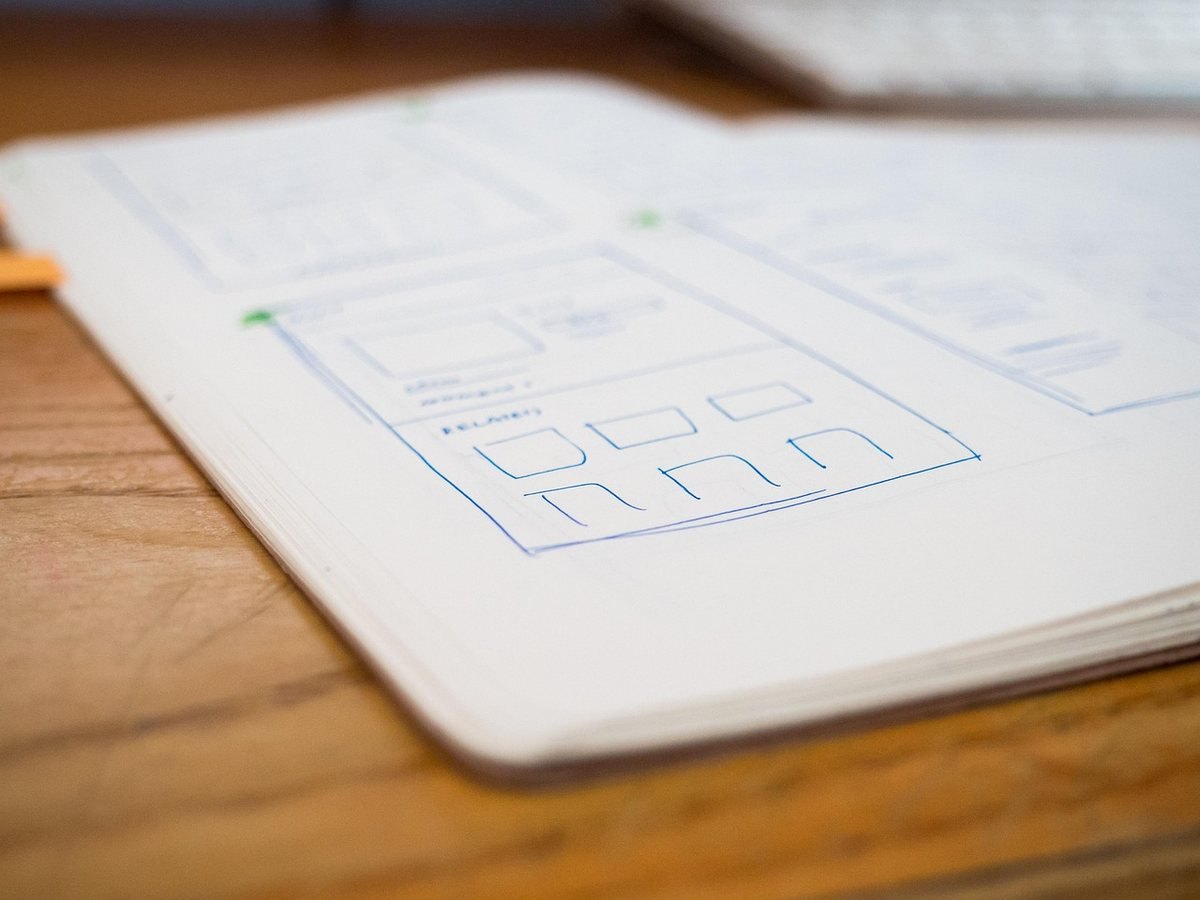 Un cahier ouvert sur une table en bois contenant des esquisses de wireframes