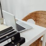 Un bureau avec ordinateur portable, tasse, dossiers et chaise en rotin