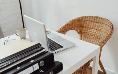 Un bureau avec ordinateur portable, tasse, dossiers et chaise en rotin