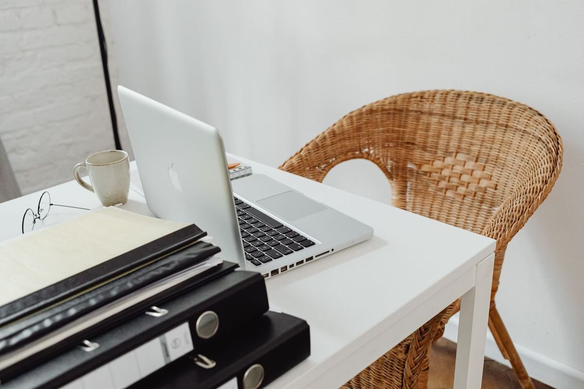 Un bureau avec ordinateur portable, tasse, dossiers et chaise en rotin