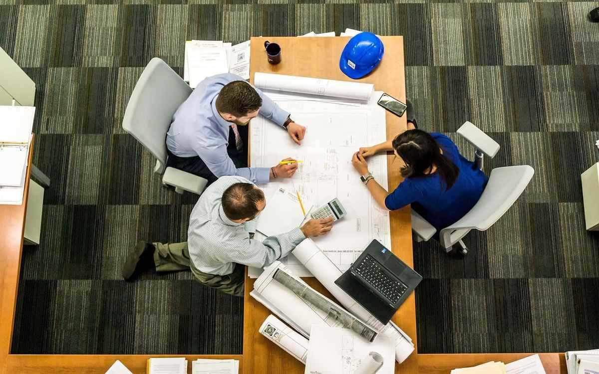 Trois collaborateurs étudient des plans sur une table de bureau