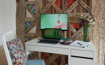 Un bureau blanc avec ordinateur, écran, chaise et vase de fleurs