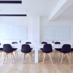 Salle claire avec table longue, chaises noires, tableau blanc et TV murale