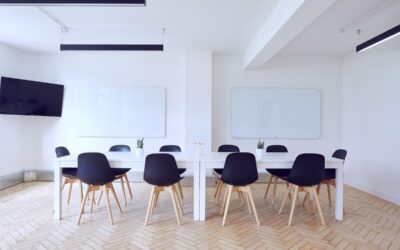 Salle claire avec table longue, chaises noires, tableau blanc et TV murale